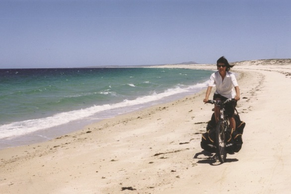 Ulrike pedaling a touring bicycle on a beach in La Ventana, Mexico.